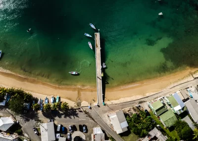 Aerial view of the Charlotteville Man of War Bay pier surrounded by fishing boats in emerald waters